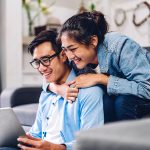 a couple on their couch at home looking at the costs of refinancing online