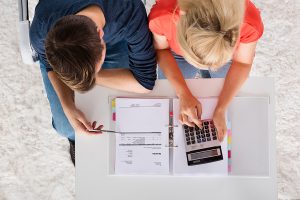 an overhead shot of a couple with a calculator and paperwork for refinancing their mortgage