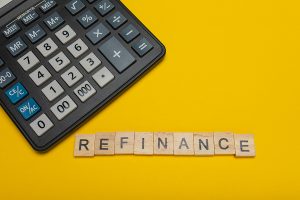 a calculator sitting on a yellow background with the word refinance spelled in block letters