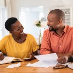 A happy African American couple review bills, pleased that automatic payments have kept their accounts up to date.