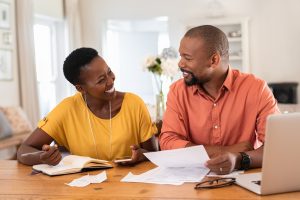 A happy African American couple review bills, pleased that automatic payments have kept their accounts up to date.