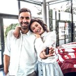 A happy couple stands in front of their new car after securing a car loan with fair credit.