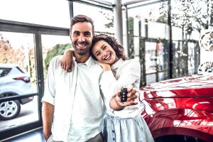 A happy couple stands in front of their new car after securing a car loan with fair credit.