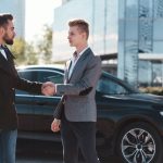 a man buys a used luxury car from a private seller and they shake hands after sealing the deal