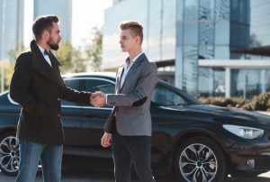 a man buys a used luxury car from a private seller and they shake hands after sealing the deal