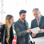 a couple talks with a salesman at the dealership about how to finance a used car