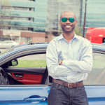 A man in sunglasses stands near his new car after answering the question, "How much car can I afford?