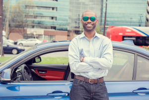 A man in sunglasses stands near his new car after answering the question, "How much car can I afford?